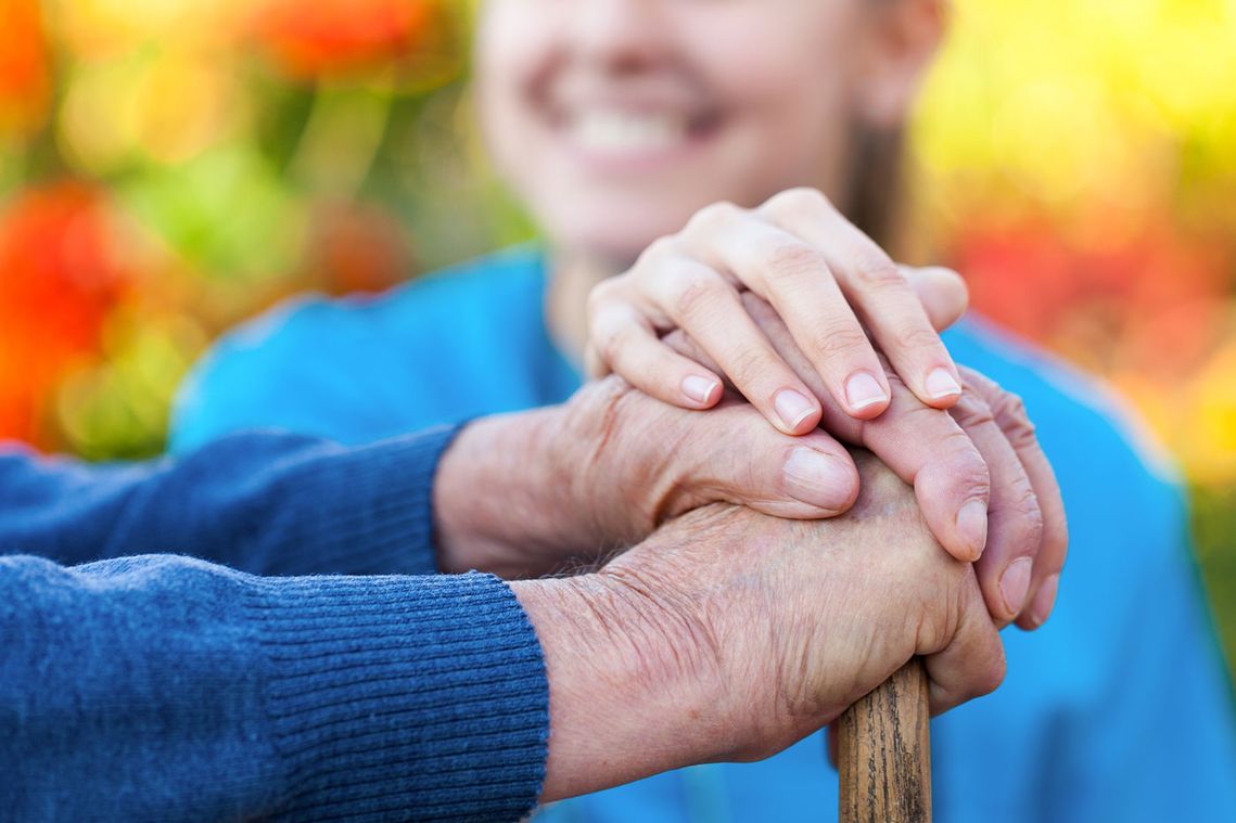 A elderly patient and a career holding hands